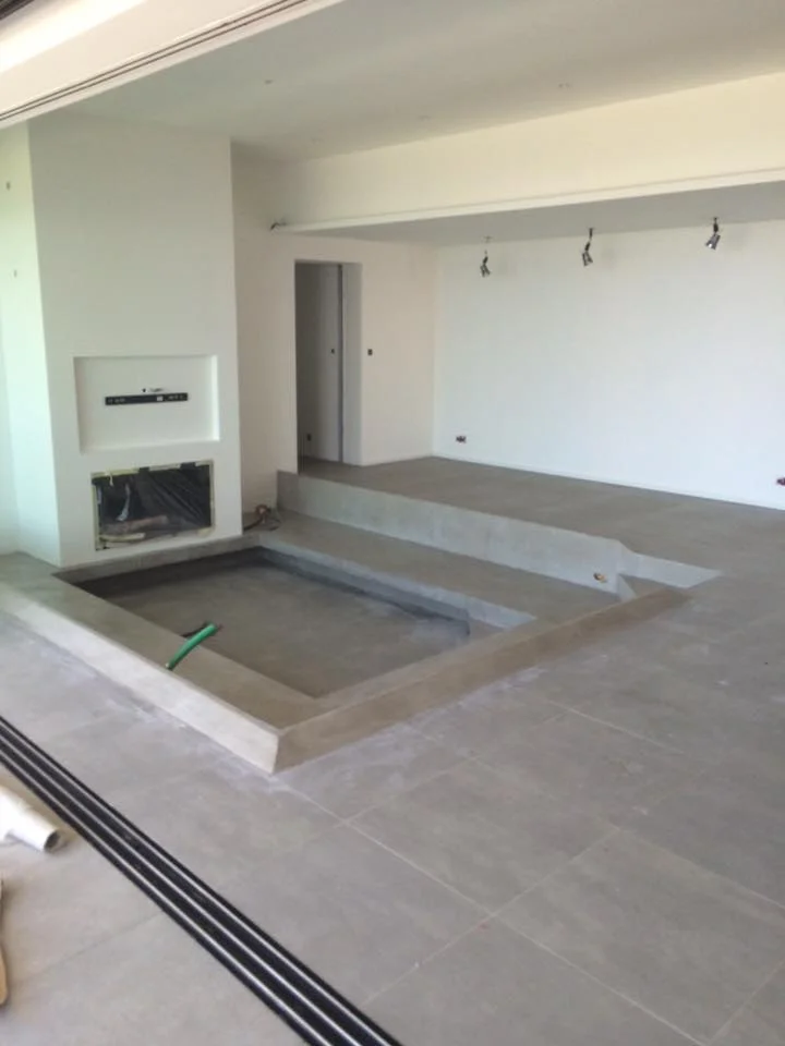 Aménagement intérieur d'un salon de villa moderne avec sol carrelé gris multi-niveaux et cheminée murale intégrée.