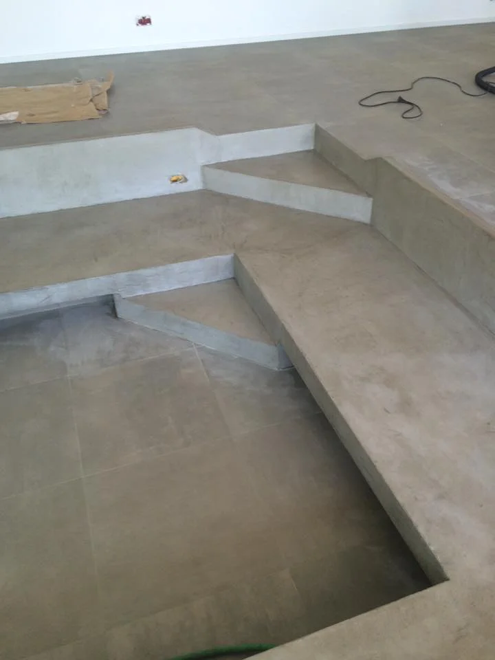 Aménagement intérieur moderne avec création de marches et plateformes en béton brut ou ciré intégré à un sol carrelé gris clair.