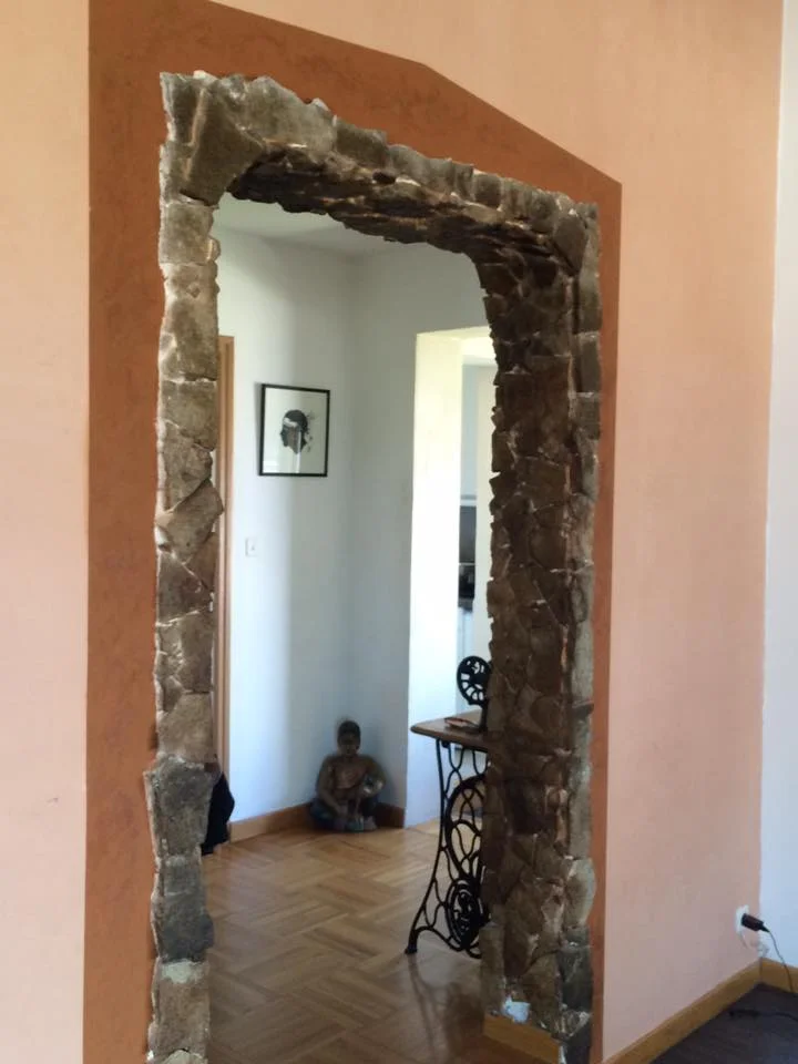 Arche décorative en enduit effet pierre brute entre deux pièces avec murs beige et ocre.
