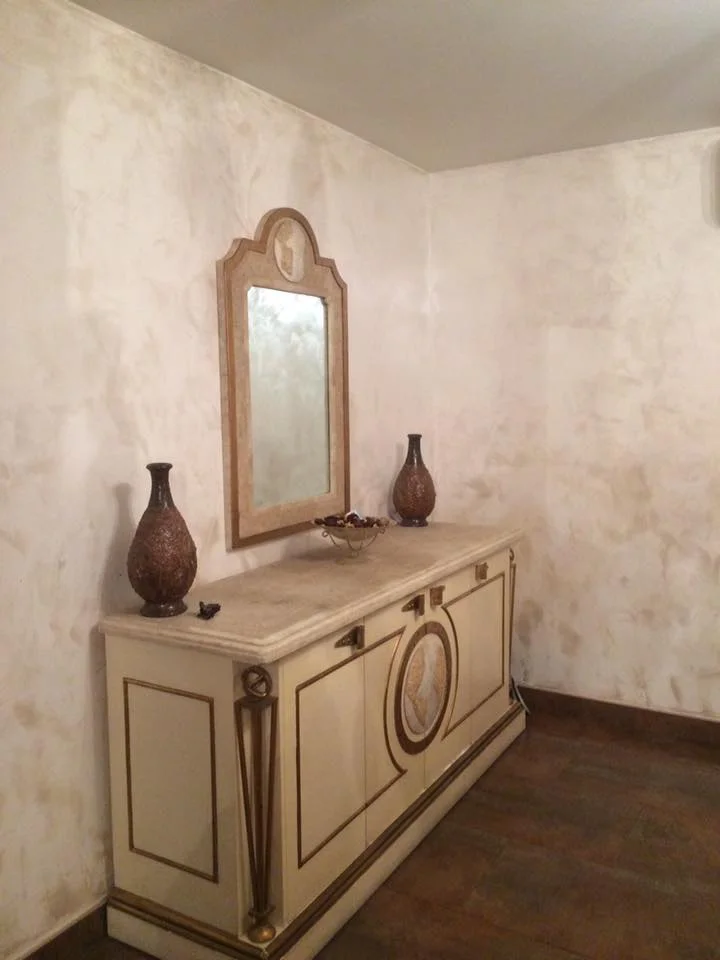 Mur intérieur avec enduit décoratif beige clair et mobilier classique.