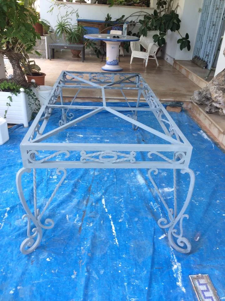 Structure de table de jardin en métal gris clair en cours de préparation et peinture sur une bâche de protection.