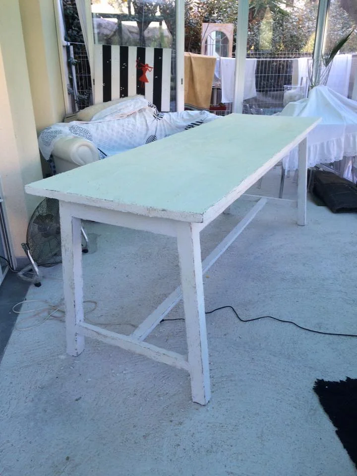 Table en bois peinte en blanc avec finition patinée dans une véranda lumineuse.